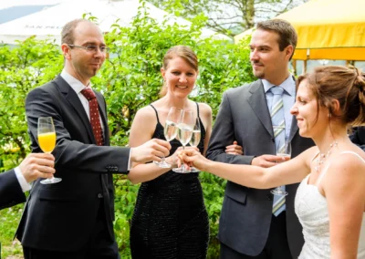 Hochzeitsfoto von Gaesten beim Anstoßen im Freien nahe Eibsee Hotel, lachend und mit Sektglaesern.