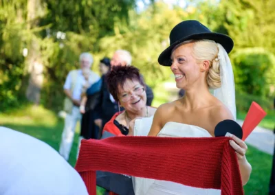Braut lacht mit rotem Schal und schwarzem Hut bei Hochzeit in Schlossgut Oberambach, Hochzeitsreportage.