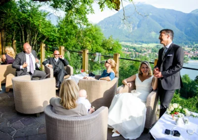 Hochzeitsgesellschaft bei Empfang im Freien, Braut lacht, Blick auf Tegernsee, Hochzeitsfoto Leeberghof.