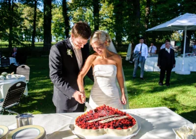 Brautpaar schneidet Hochzeitstorte im Freien bei einer Hochzeitsfeier in Schlossgut Oberambach. Hochzeitsfotografie.