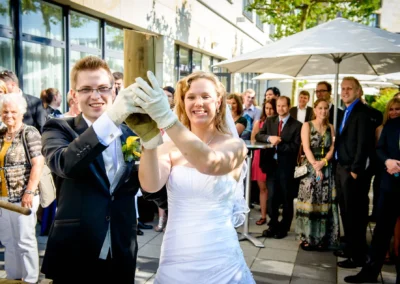 Brautpaar zersägt Holz bei Hochzeitsfeier in Starnberg. Hochzeitsreportage mit Gästen im Hotel 4 Jahreszeiten.