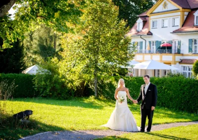 Brautpaar in eleganter Hochzeitsfotografie vor Schlossgut Oberambach, umgeben von grüner Natur und Sonne.