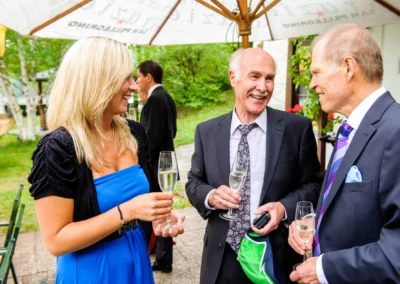 Gäste bei einer Hochzeit im Eibsee Hotel, Grainau, lächelnd beim Anstoßen mit Champagnergläsern im Freien.