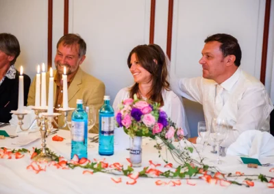 Hochzeitsgesellschaft am Tisch mit Blumenstrauss in Starnberg, lachend und kerzenbeleuchtet, Hochzeitsreportage.