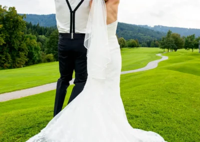 Brautpaar hebt Arme bei Hochzeitsfotografie nahe Tegernsee. Romantisches Portrait im Gruenen mit Brautkleid und Schleier.
