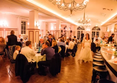 Hochzeitsfeier in einem eleganten Saal am Starnberger See, Gaeste sitzen an Tischen, Braut geht umher.