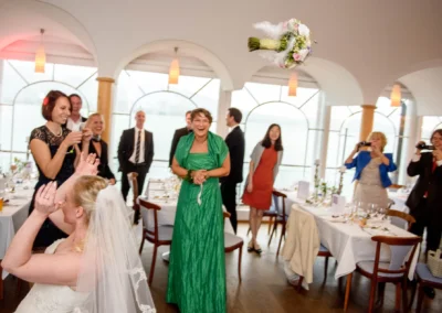 Braut wirft Blumenstrauss bei Hochzeit am Tegernsee, Gaeste lachen, Cafe Kreutzkamm. Hochzeitsreportage mit emotionalen Momenten.