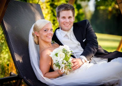 Brautpaar entspannt auf Liegestuhl, lachend im Garten von Schlossgut Oberambach. Hochzeitsfoto bei Starnberger See.