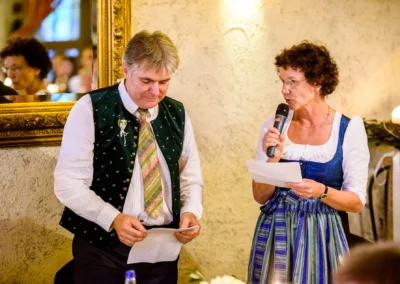 Redner bei Hochzeit im Hofgut zur Mühle, traditionell gekleidet, spricht in Mikrofon, Hochzeitsfotografien.