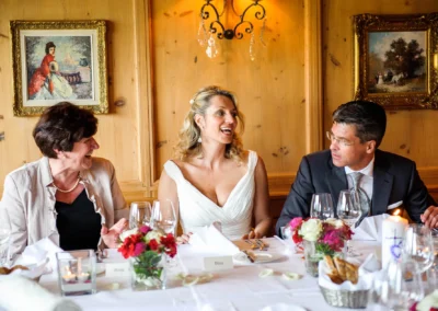 Braut mit zwei Gaesten bei der Hochzeit im Leeberghof Tegernsee, geschmueckter Tisch mit Blumen und Kerzen.