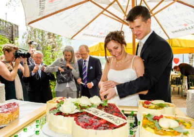 Brautpaar schneidet Hochzeitstorte bei Feier am Eibsee; Hochzeitsfotografie dokumentiert freudigen Moment.