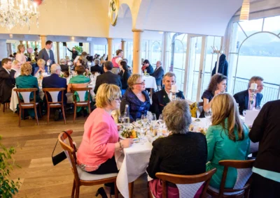 Hochzeitsfoto: Gäste sitzen an gedeckten Tischen bei einer Feier im Cafe Kreutzkamm am Tegernsee. Festliche Atmosphäre.