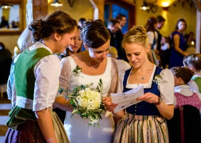 Braut mit zwei Freundinnen in Trachtenkleidern beim Lesen eines Dokuments in Hofgut zur Muehle Hochzeit.