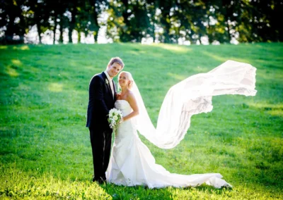 Brautpaar bei Hochzeit auf Wiese in Oberambach mit wehenden Schleier im Hintergrund, Hochzeitsfotografie.