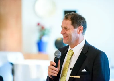 Ein Mann in Anzug und Krawatte haelt Mikrofon bei einer Hochzeitsfeier im Hotel 4 Jahreszeiten Starnberg.