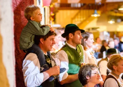 Gäste in Tracht bei einer Hochzeit in Hofgut zur Muehle. Ein Mann mit Kind auf den Schultern. Hochzeitsreportage.