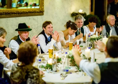 Gäste einer Hochzeit zwischen München und Rosenheim sitzen lachend am Tisch bei Kerzenlicht. Hochzeitsfotografie.