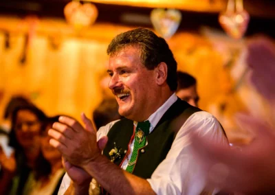 Ein Mann lacht und klatscht auf einer Hochzeit im Hofgut zur Muehle. Hochzeitsszene mit Freude und Tradition.