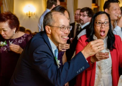 Gäste lachen und genießen Getränke bei einer Hochzeitsfeier, südlich Rosenheim. Hochzeitsfotograf fängt den Moment ein.