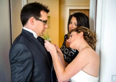 Bräutigam wird bei Hochzeit am Starnberger See von zwei Frauen beim Anziehen der Ansteckblume unterstützt. Hochzeitsfotograf.