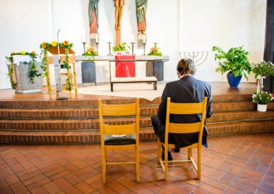Ein Mann im Anzug sitzt auf einem Stuhl vor dem Altar in der Friedenskirche Dachau bei einer kirchlichen Trauung.