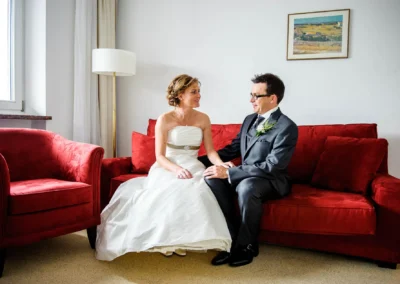 Brautpaar sitzt auf rotem Sofa, Hochzeitsfoto, aufgenommen bei Hochzeit in Harkirchen, Hochzeitsportraits innen.