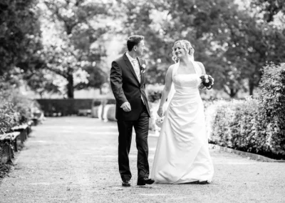 Brautpaar bei Hochzeitsfotos im Hofgarten München, Hand in Hand spazierend, Schwarzweiß-Aufnahme.