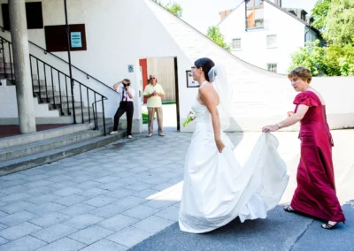 Braut im weissen Kleid mit Dame in Rot bei kirchlicher Trauung in Friedenskirche Dachau, Hochzeitsfotografie.