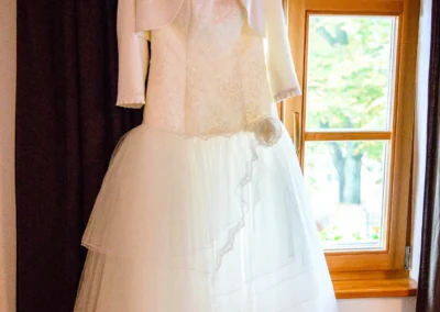 Weißes Brautkleid mit Jacke vor Fenster bei Hochzeit in Landshut fotografiert. Hochzeitsfotografie aus Muenchen.