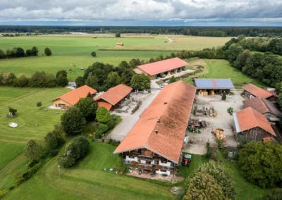 Luftaufnahme einer Hochzeit auf einem Bauernhof bei Holzkirchen mit roten Dächern und grünen Wiesen. Hochzeitsfotografie.