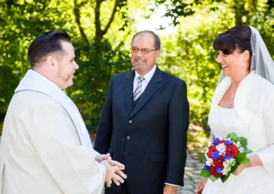Brautpaar und Priester lachen im Garten bei Hochzeit Christuskirche Gauting nahe Muenchen, Hochzeitsfotografie.