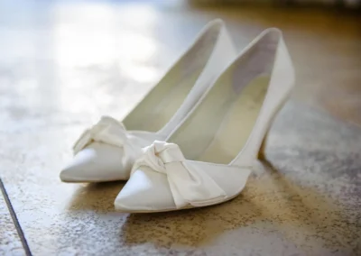 Hochzeit in nahe dillingen: Elegante weisse Brautschuhe mit Schleifen auf Fliesenboden bei der Hochzeitsfotografie.