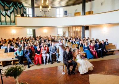 Kirchliche Trauung bei Hochzeit in Friedenskirche Dachau, Brautpaar und Gaeste in Sitzreihen, Hochzeitsreportage.