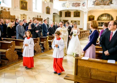 Brautpaar bei kirchlicher Trauung mit Pfarrer in Heilig-Geist-Kirche Neuburg, umgeben von Gaesten. Hochzeitsfotografie.