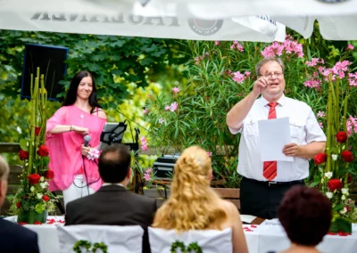 Hochzeitsreportage freie Trauung im Dachauer Hinterland, Rednerin mit Mikrofon, Blumenarrangement aus Rosen.