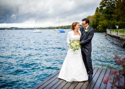 Brautpaarfoto am Steg des Starnberger Sees, Hochzeitsfotografie in natuerlicher Umgebung mit Blumenschoens.