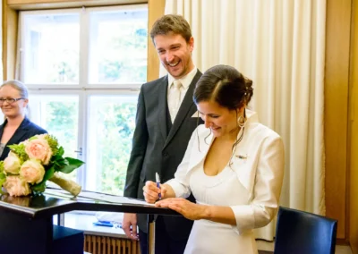 Brautpaar unterschreibt bei der standesamtlichen Trauung im Standesamt Mandlstrasse Muenchen, Hochzeitsfoto.