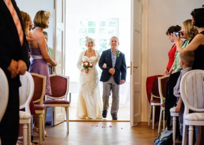 Braut und Begleiter betreten Raum zur standesamtlichen Trauung im Kurhaus Bad Toelz, umgeben von Gaesten. Hochzeitsfoto.