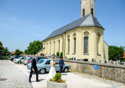 Brautpaar vor Kirche St. Johann-Baptist Irschenberg, Hochzeitsfotografie in sommerlicher Umgebung im Landkreis Miesbach.