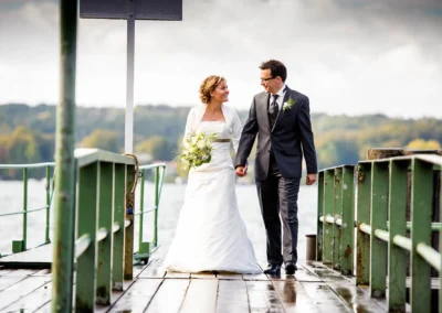 Brautpaar geht Hand in Hand auf einem Steg am Starnberger See, Hochzeitsportrait mit See im Hintergrund.