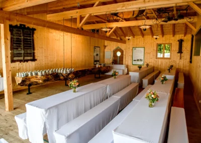 Hochzeit im Archehof Schlickenrieder Otterfing, geschmueckter Saal mit Blumenarrangements auf Tischen.