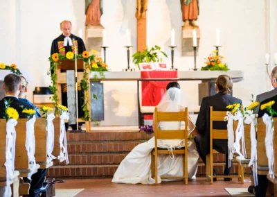 Hochzeit in der Friedenskirche Dachau, Brautpaar sitzt vor dem Altar, dekoriert mit Kerzen und Blumen, Hochzeitsreportage.