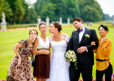 Brautpaar und Gaeste mit lustigen Gesichtern im Schlossgarten bei einer Hochzeitsreportage in Nymphenburg, Muenchen.