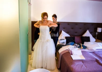Braut beim Getting Ready in Hotelzimmer, Landshut, Hochzeitsfotografie zeigt Helferin beim Kleid anziehen.