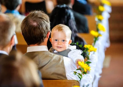 Kleinkind auf dem Schoß eines Mannes während einer kirchlichen Trauung, Hochzeit nördlich von München, Sonnenblumen.