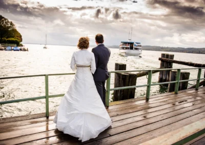 Brautpaar am Steg blickt auf Schiff bei Hochzeit am Starnberger See, festgehalten in Hochzeitsportrait.