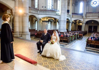 Brautpaar bei kirchlicher Trauung in Kirche St. Lukas Muenchen, Gaeste in Sitzreihen, Hochzeitsfotografie.