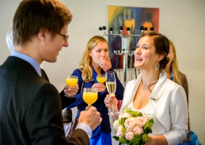 Brautpaar diskutiert im Standesamt Mandlstrasse mit Gaesten ueber die Trauung, Teil einer Hochzeitsreportage in Muenchen.
