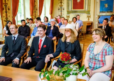 Gäste und Paar bei standesamtlicher Trauung, lachend im Schloss Ismaning. Hochzeitsreportage von Fotograf in München.