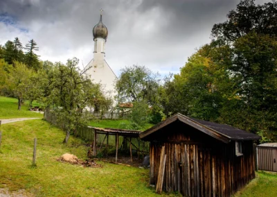Kirche mit Zwiebelturm bei einer Hochzeit am Starnberger See, umgeben von Baeumen und einem Gartenhaus.